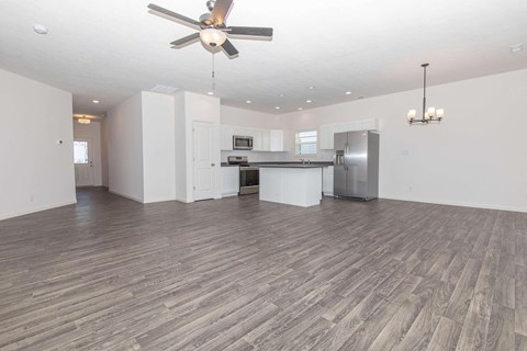 an empty living room with a kitchen and a ceiling fan