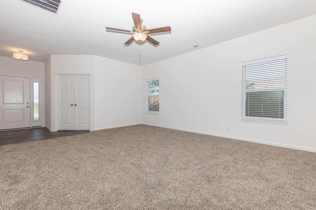 an empty living room with a ceiling fan and a window