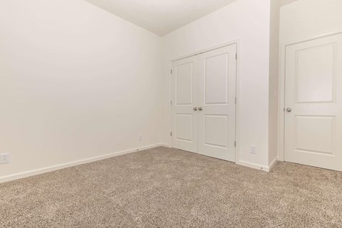 a bedroom with white walls and carpet and two doors