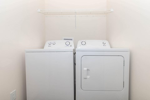 a washer and dryer in a room with a white wall and a shelf