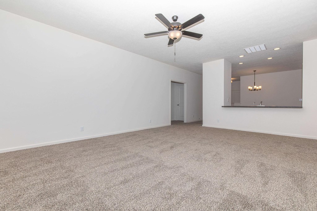 an empty living room with a ceiling fan and white walls
