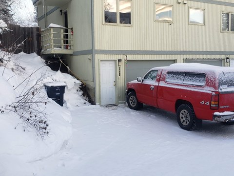 a red truck parked in the snow in front of a house