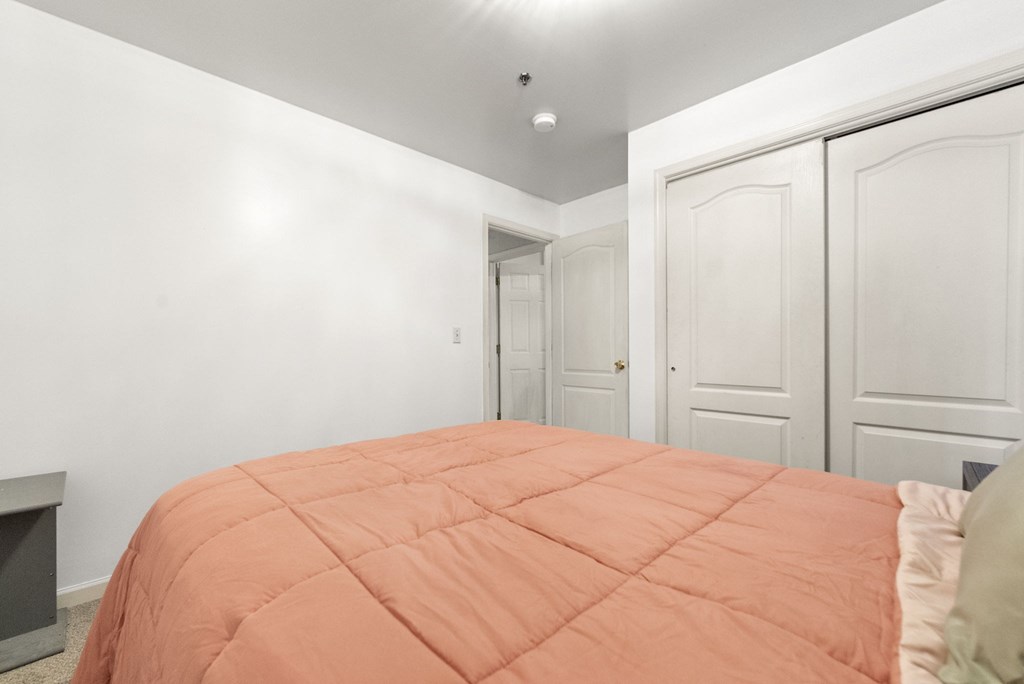 a bedroom with white walls and a bed with an orange comforter
