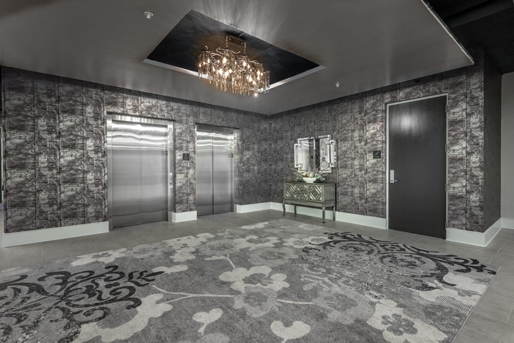 a lobby with elevators and a rug and a chandelier