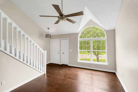 an empty living room with a large window and a ceiling fan