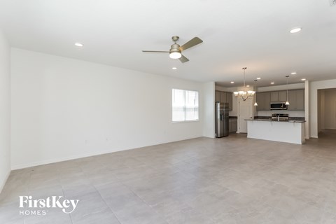 A spacious empty room with a fan and a kitchen in the background.