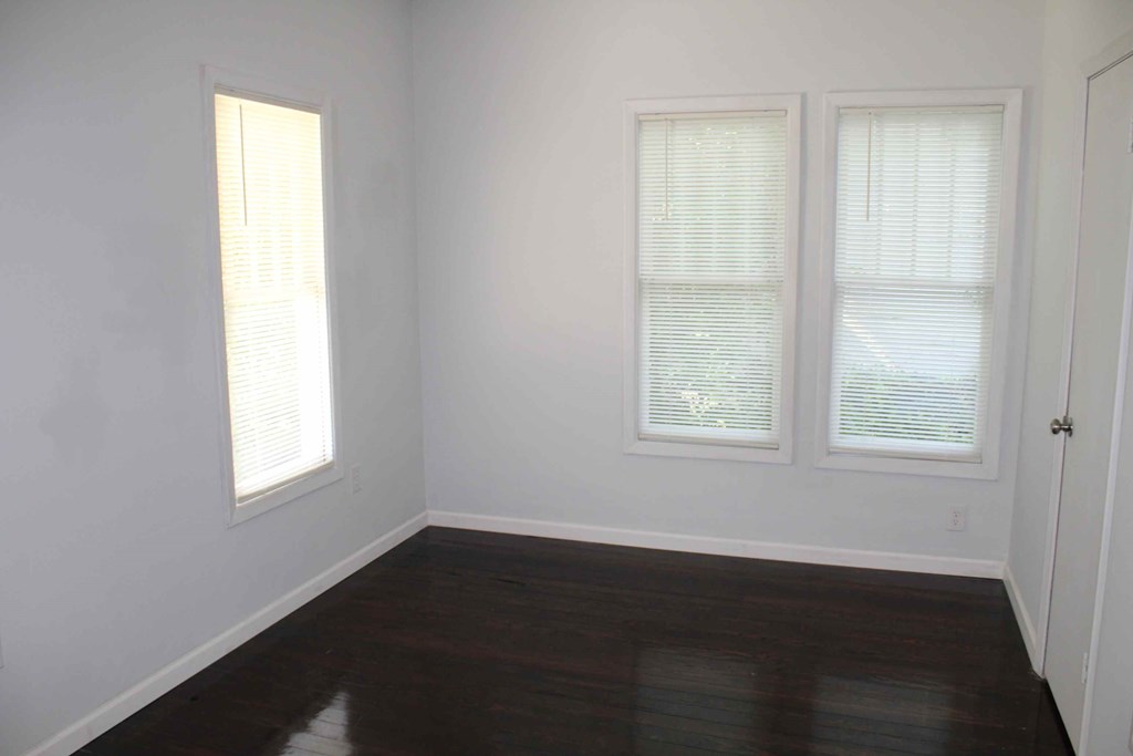 an empty room with white walls and wood floors and two windows