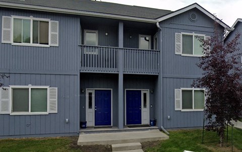 A grey two story house with a balcony and blue doors.