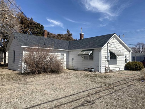 a small white house with a gray roof on a field