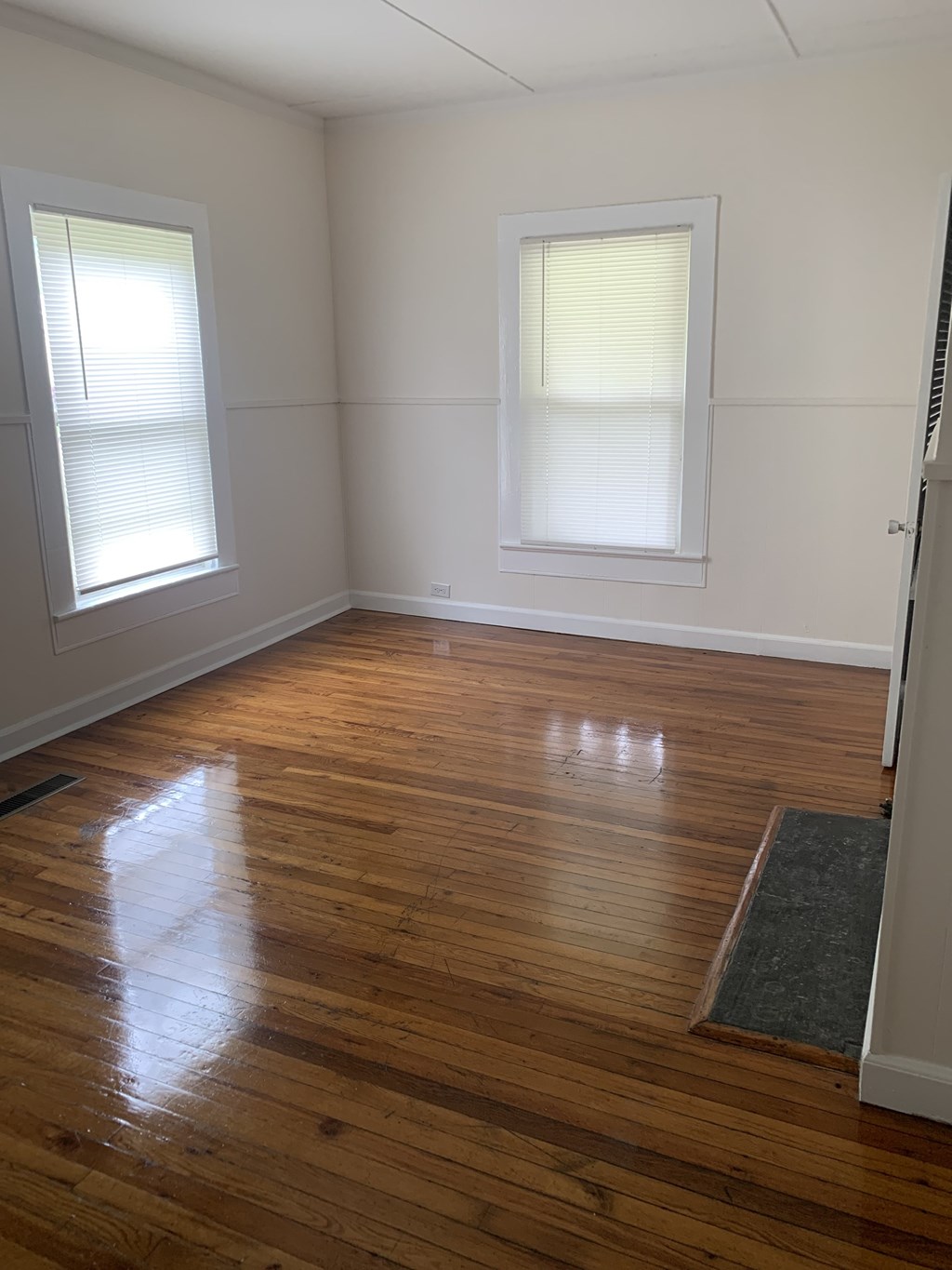 an empty room with wooden floors and two windows