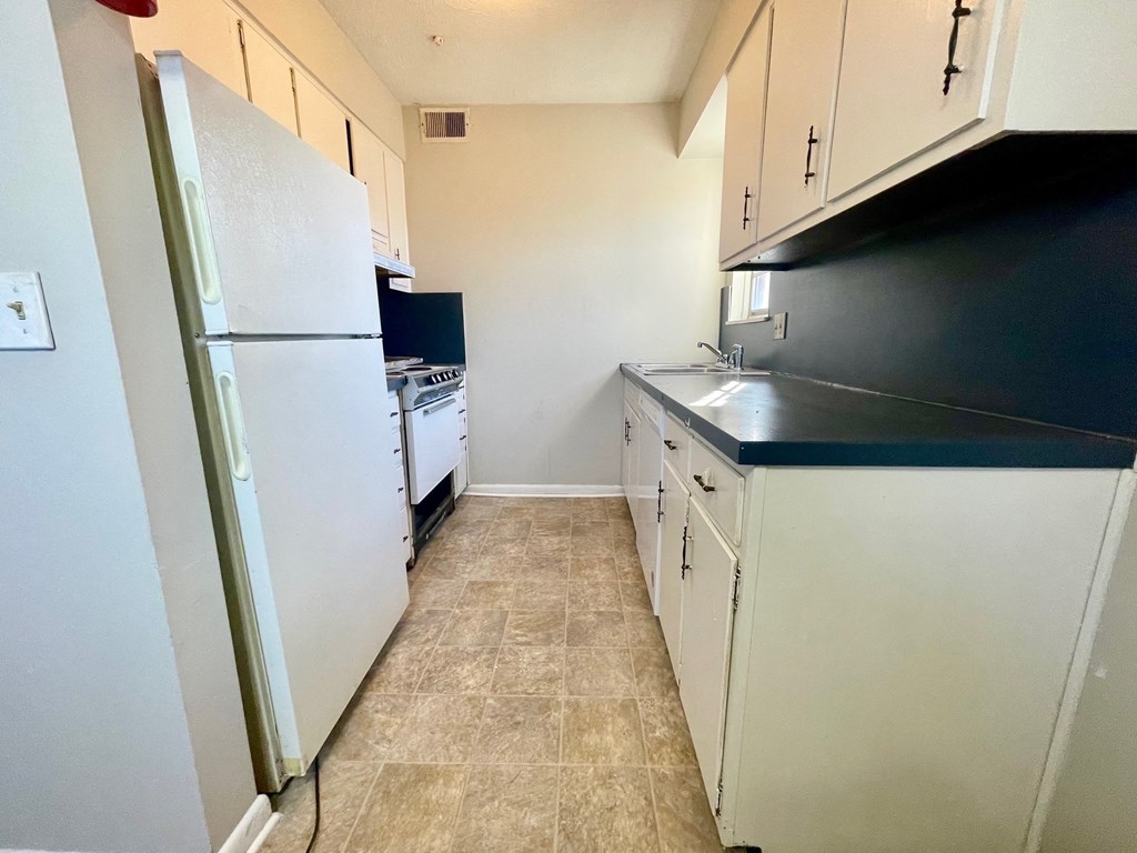 A kitchen with a white refrigerator and white cabinets.