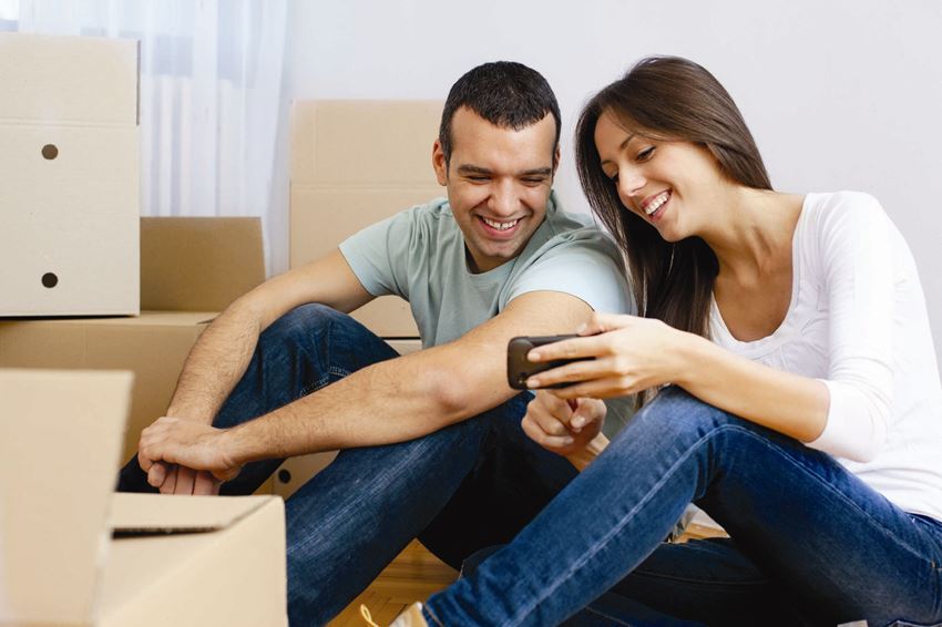 a man and woman sitting on the floor looking at a cell phone