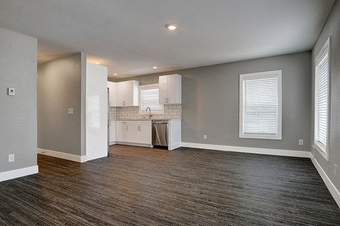 an empty living room with a kitchen with white cabinets