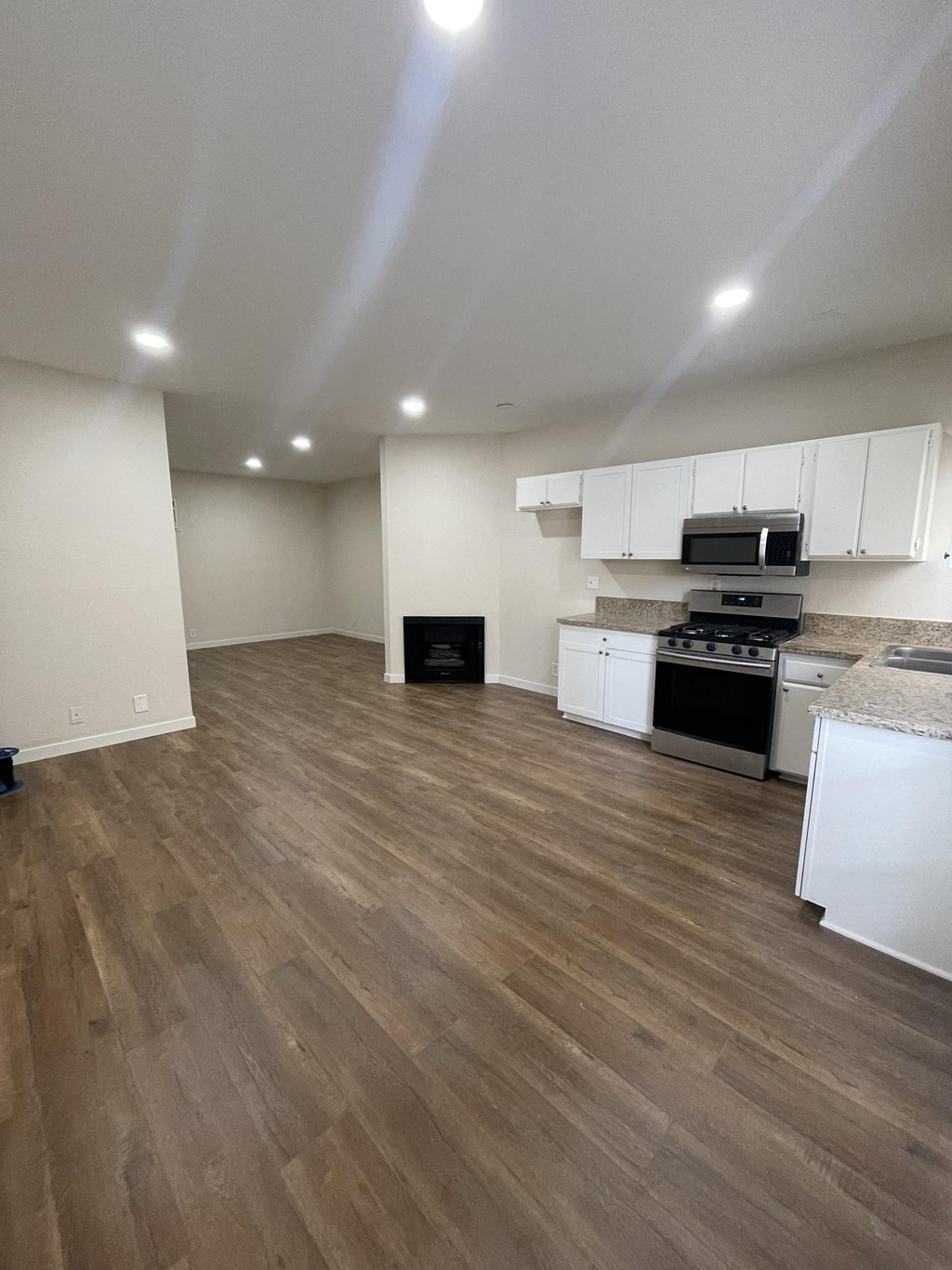 an empty kitchen and living room with wood flooring and white cabinets