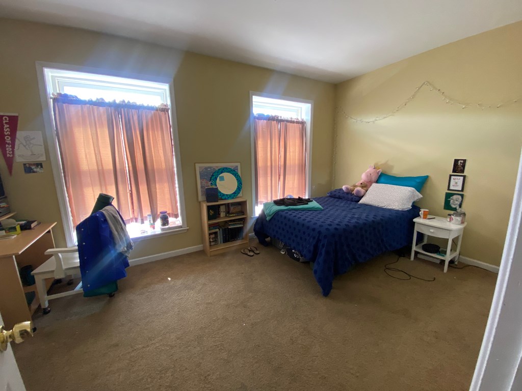 a bedroom with a bed and a desk and two windows