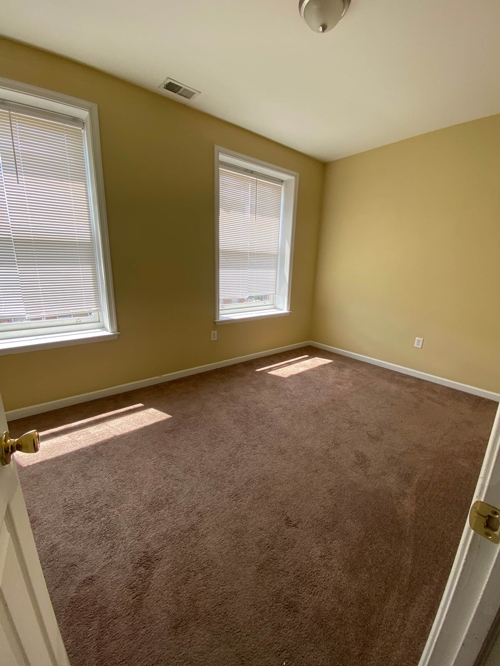 a carpeted room with two windows and a door
