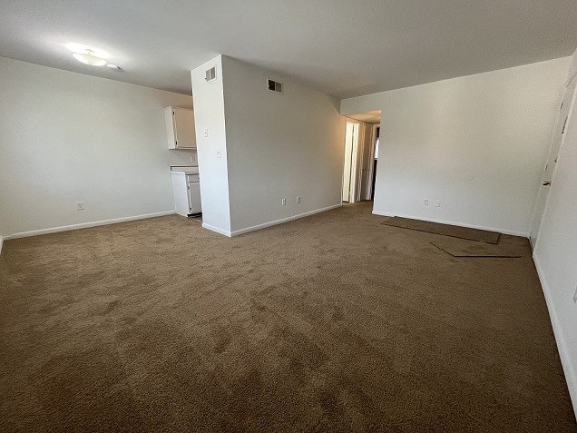 an empty living room with carpet and a kitchen