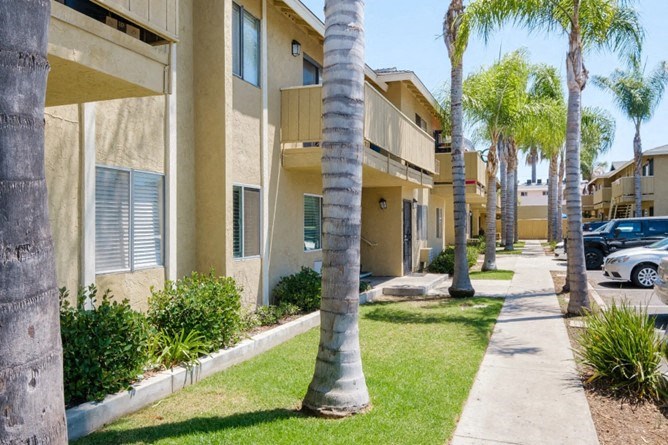 an apartment building with palm trees and a sidewalk