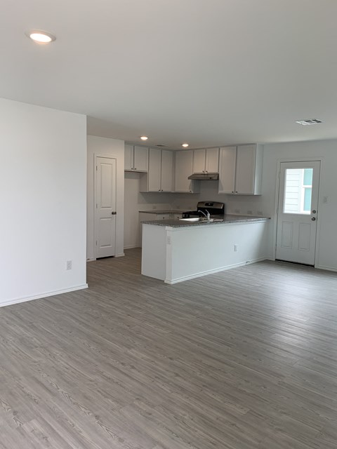 an empty living room and kitchen with white walls and wood flooring