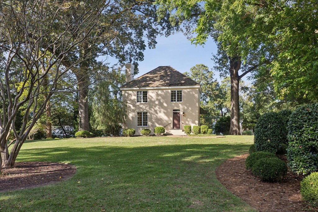 A house with a brown roof and white walls is surrounded by green trees and bushes.