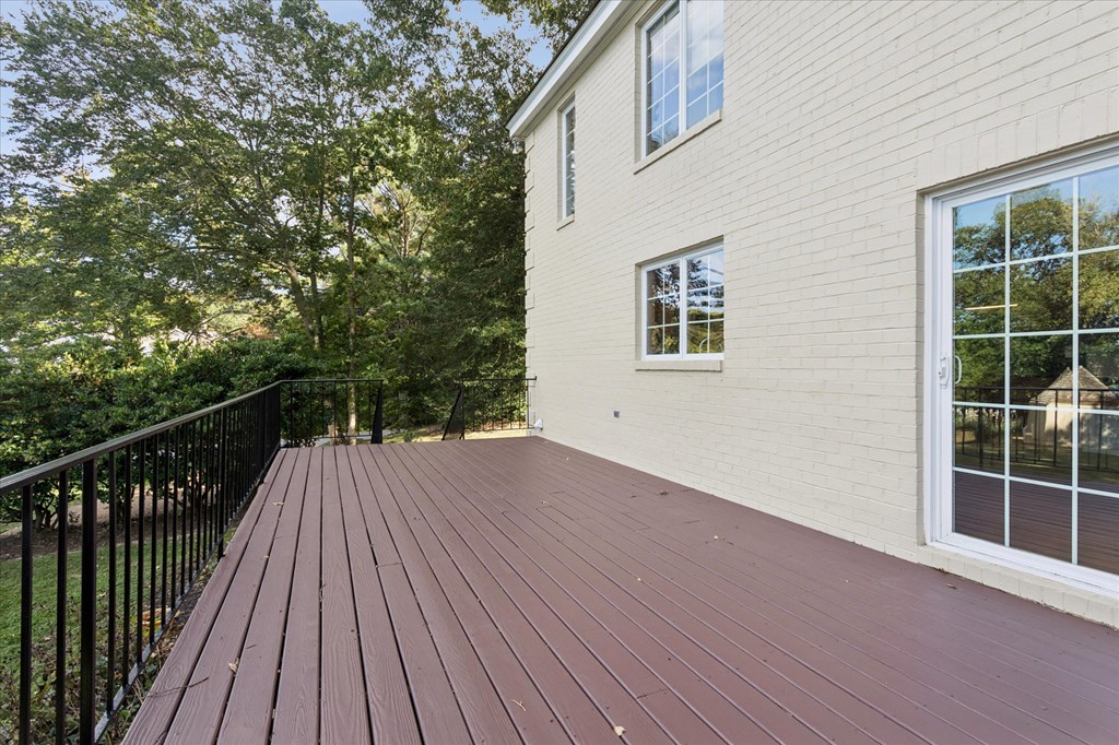 A wooden deck with a black railing and a white house in the background.