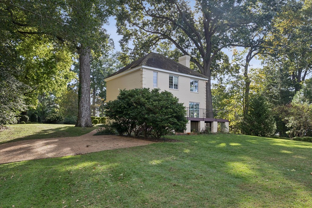 A house with a white roof and a yellow wall is surrounded by trees.