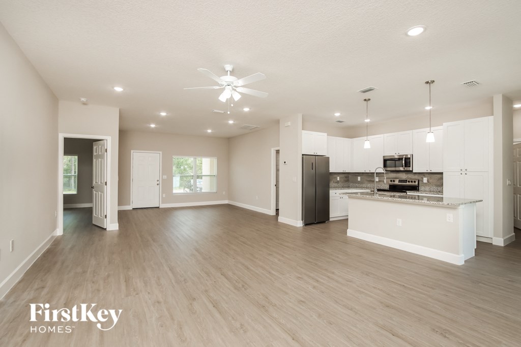 an open kitchen and living room with white cabinets and a stainless steel refrigerator