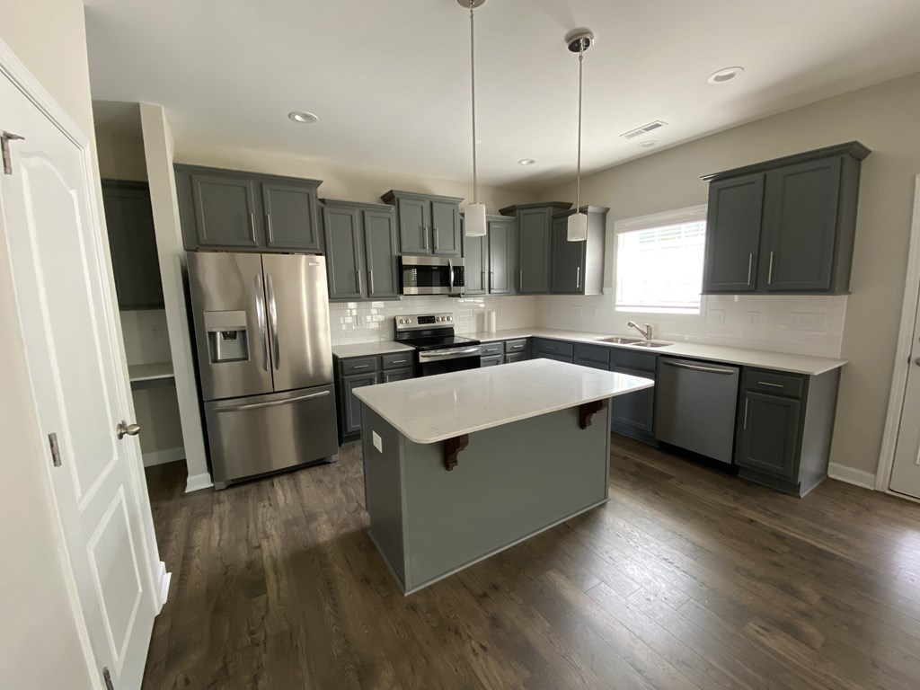 A kitchen with a refrigerator, microwave, oven, and sink.