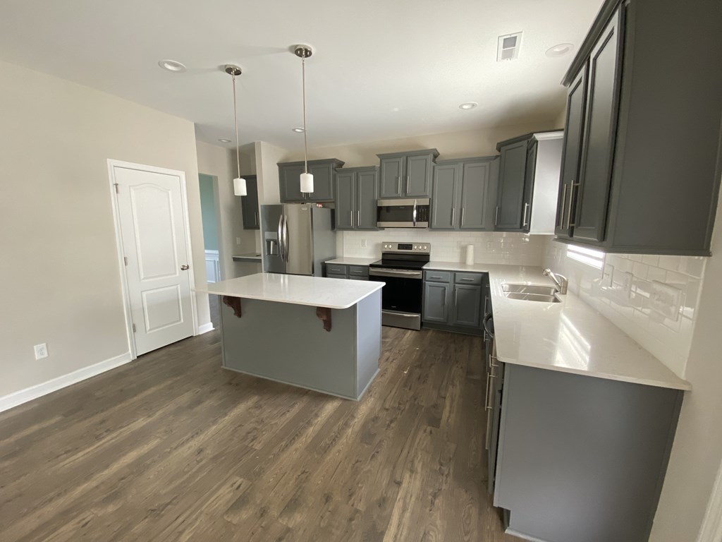 A kitchen with a white counter top and wooden floors.