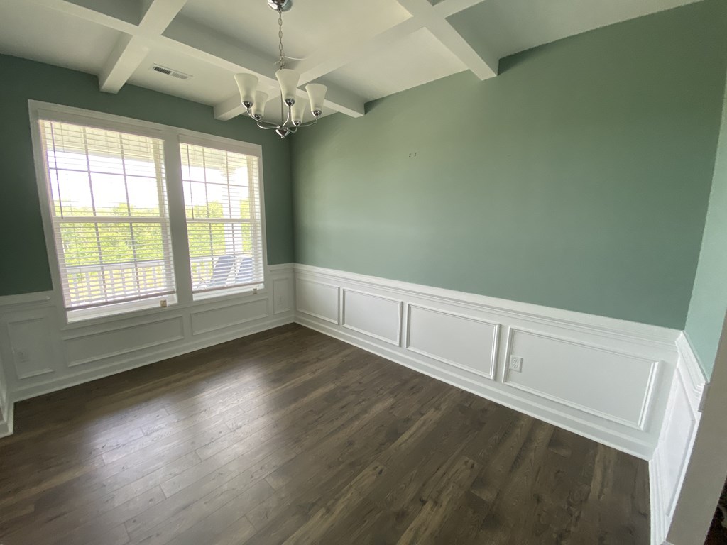 A room with a chandelier, wooden floors, and white trim.