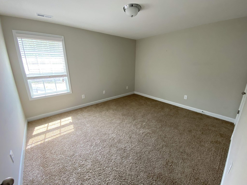 A room with a carpeted floor and a window letting in sunlight.