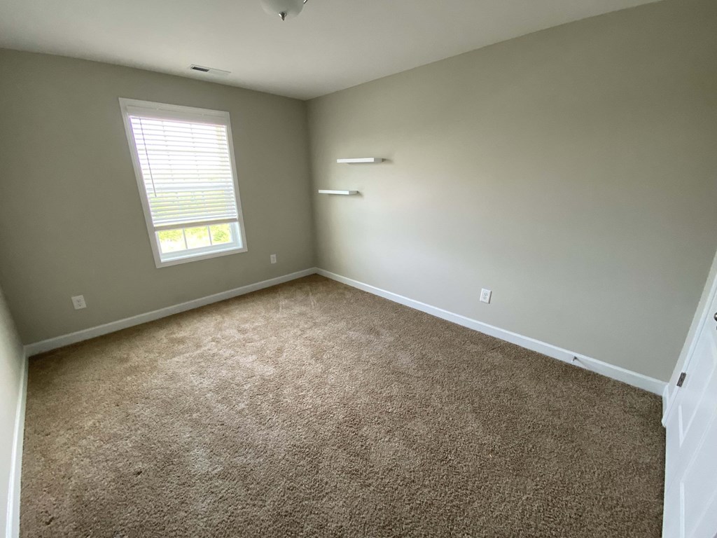 A room with a carpeted floor and a window with blinds.