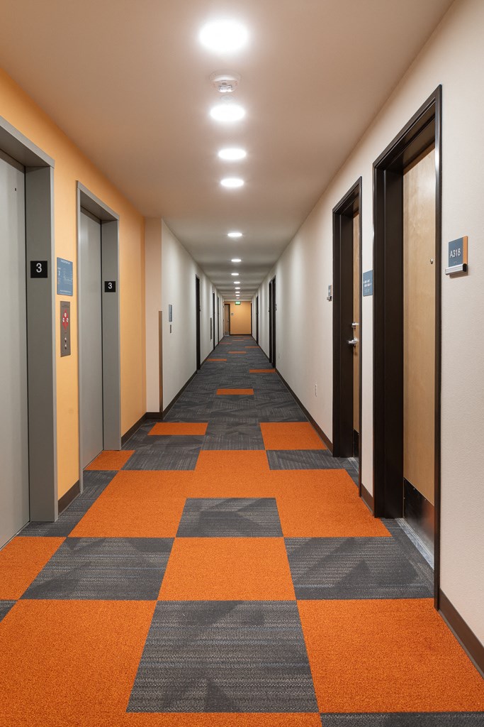 a corridor with doors and orange and gray carpet in a building