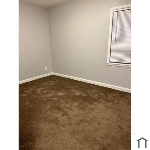 A room with a carpeted floor and a window with blinds.