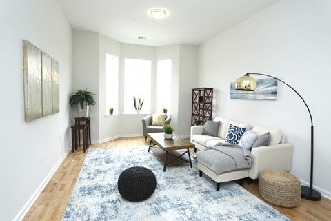 A living room with a white couch, a black ottoman, and a blue rug.
