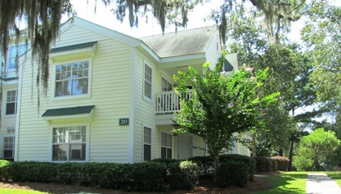 A white building with a balcony and a tree in front of it.