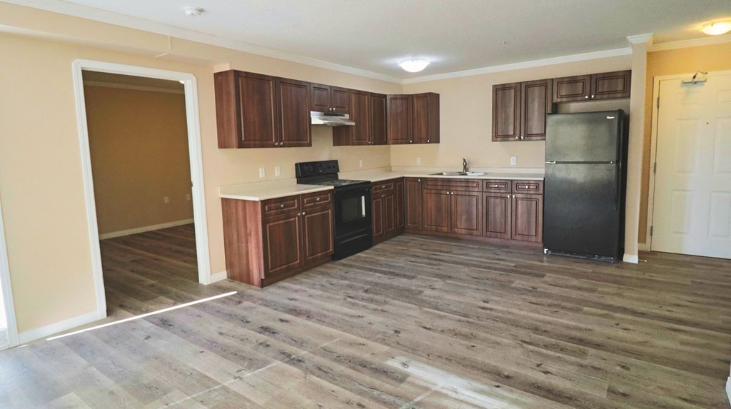 an empty kitchen with wooden floors and cabinets and a black refrigerator