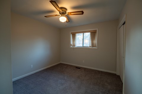 A room with a ceiling fan and a window with curtains.