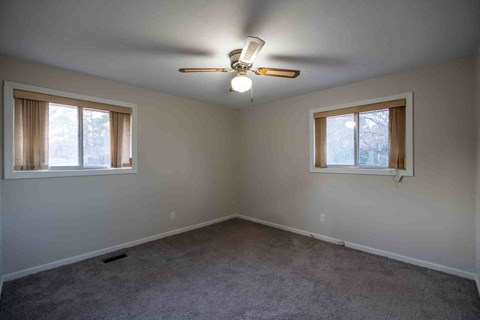 A room with a ceiling fan and two windows.