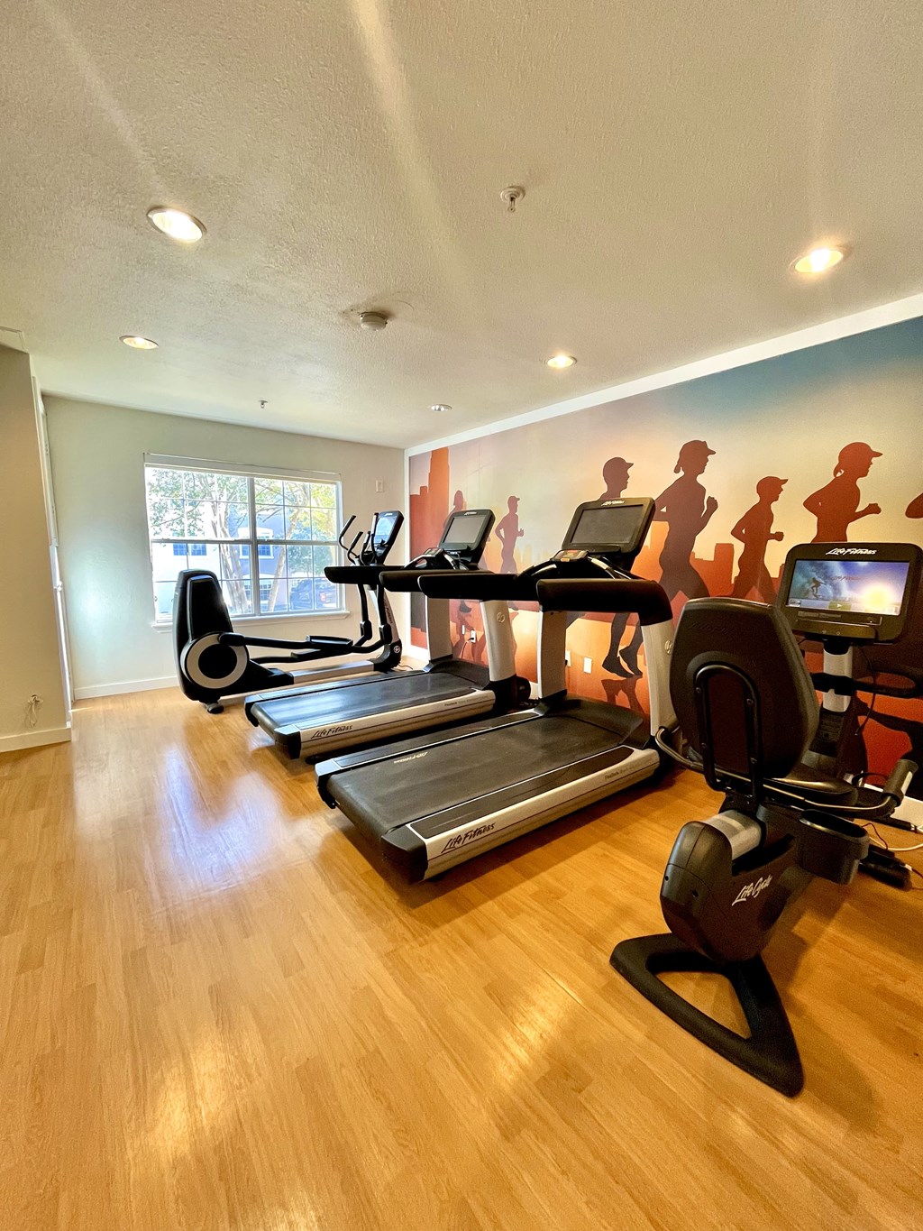 a gym with cardio equipment and a wall mural of violence