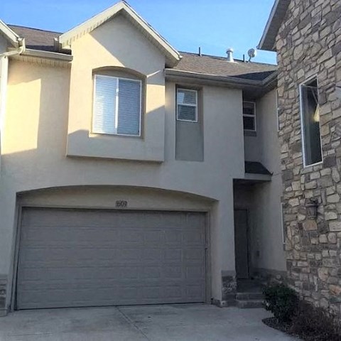 A two-story house with a garage door and a stone wall.