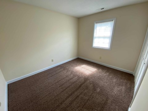A room with a brown carpet and a window.