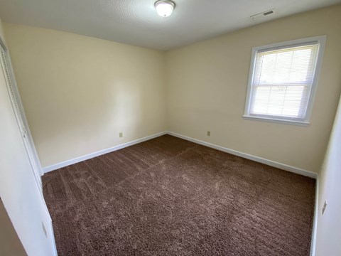 A room with a carpeted floor and a window with blinds.