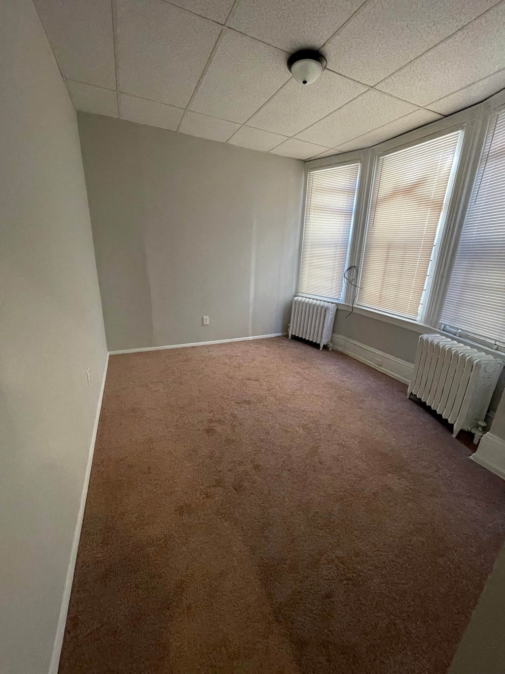 an empty room with a carpet and three windows