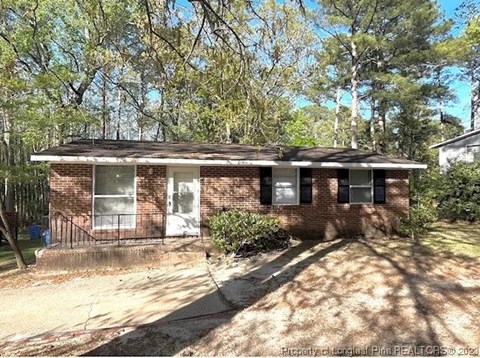 A house with a white door and windows is surrounded by trees.