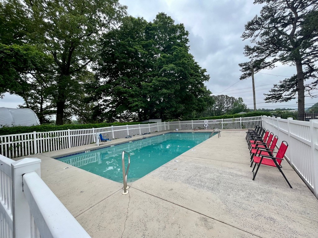 a resort style pool with red chairs and trees