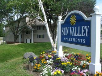 a sign for sun valley apartments in front of a yard of flowers