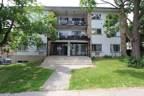 the front of an apartment building with a lawn and trees