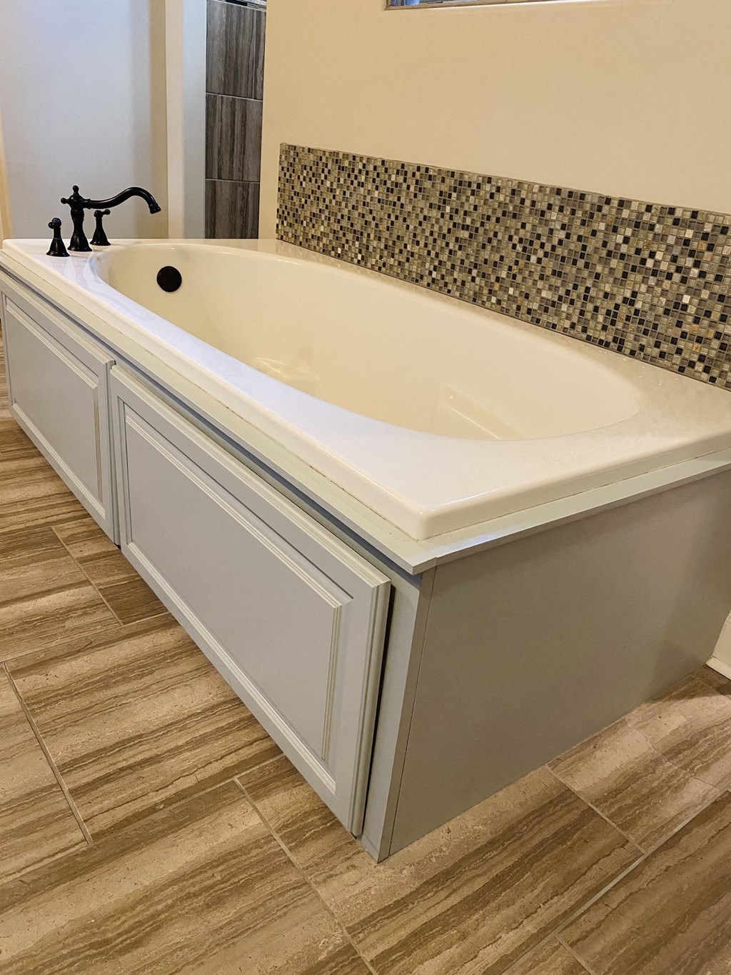 a large bath tub in a bathroom with white cabinets and a tiled wall