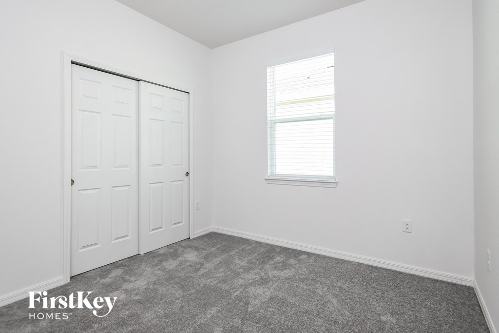 a bedroom with white walls and carpet and a window and white doors